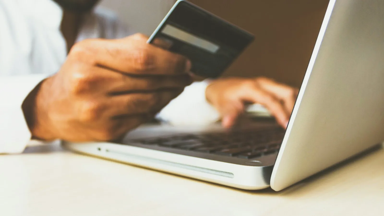 Une personne tient une carte bancaire devant un ordinateur portable pour régler un achat en ligne